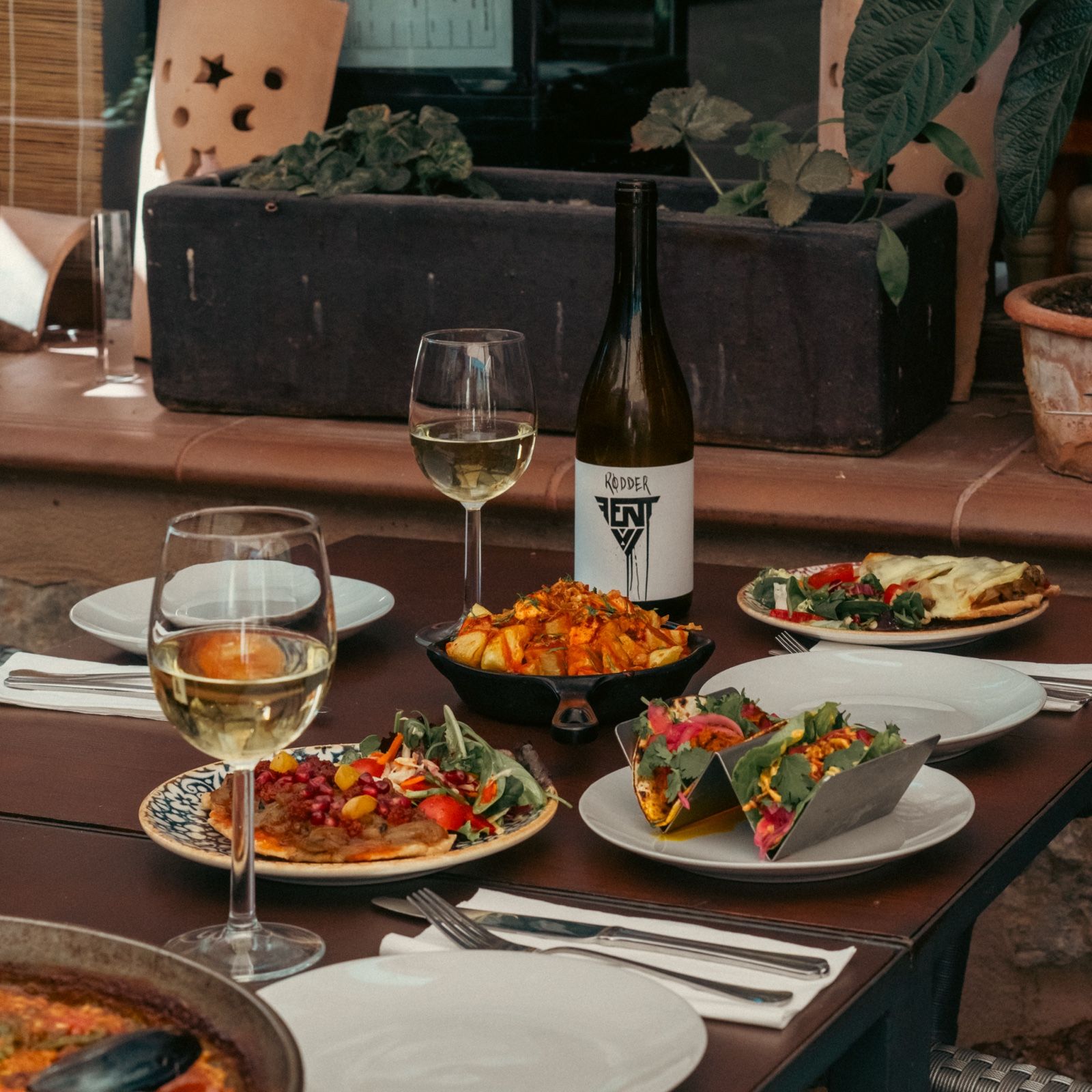 Mesa surtida con tapas, tacos, ensalada y vino en la terraza del Bar Molino, Sóller