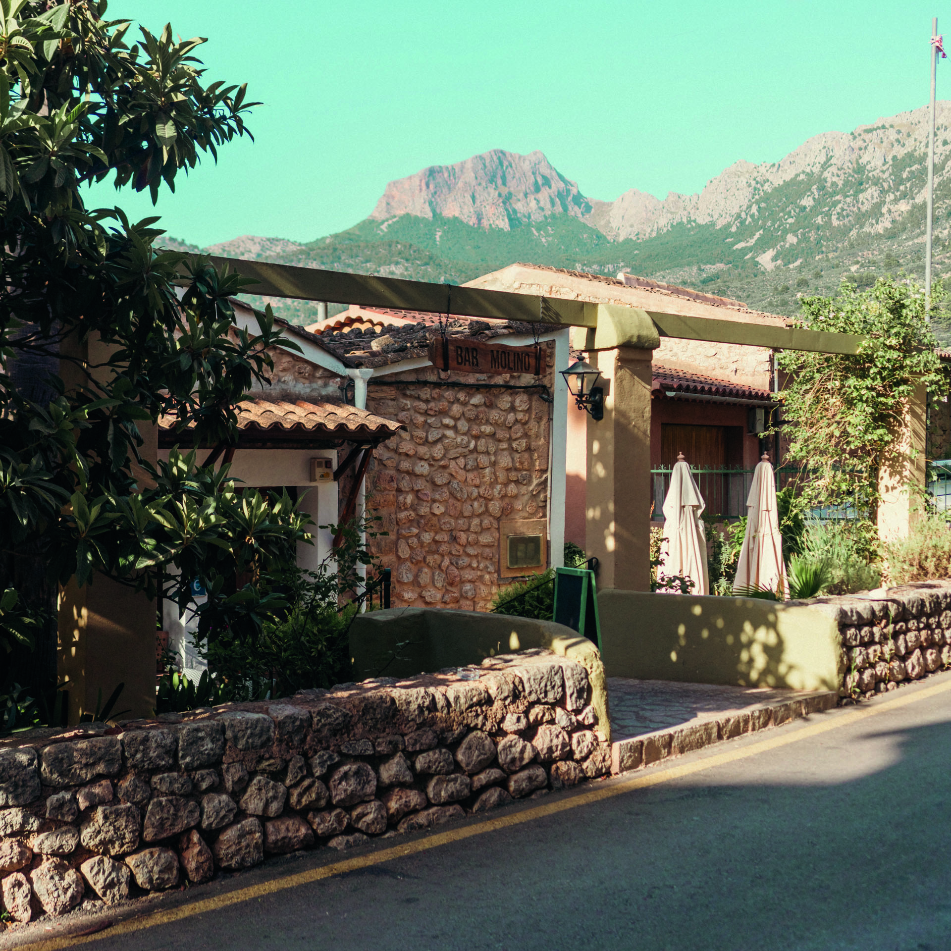 Fachada de piedra del Bar Molino con la Sierra de Tramuntana al fondo, Sóller